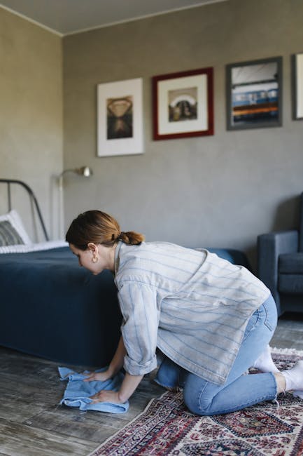 A person holding a yellow portable industrial carpet cleaning machine, focusing on the device with a black ventilation grille and control panel, while working on a patterned area rug in an indoor sett
